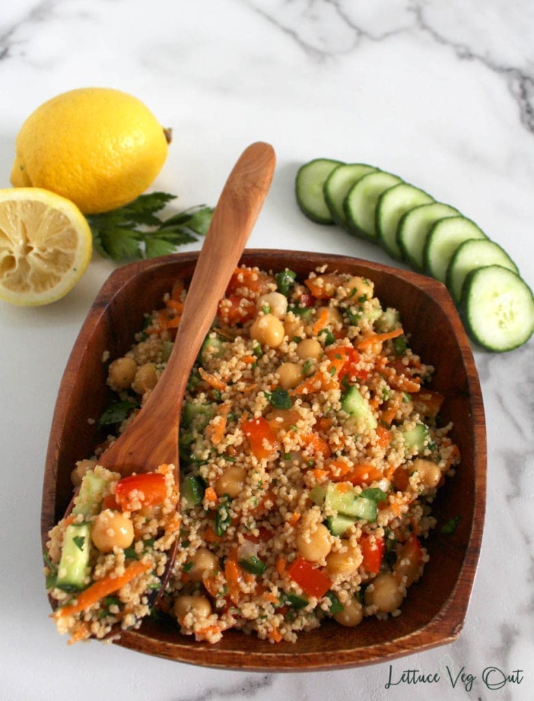 Overhead view of square wooden bowl of vegan couscous chickpea salad with spoonfull of salad resting on top