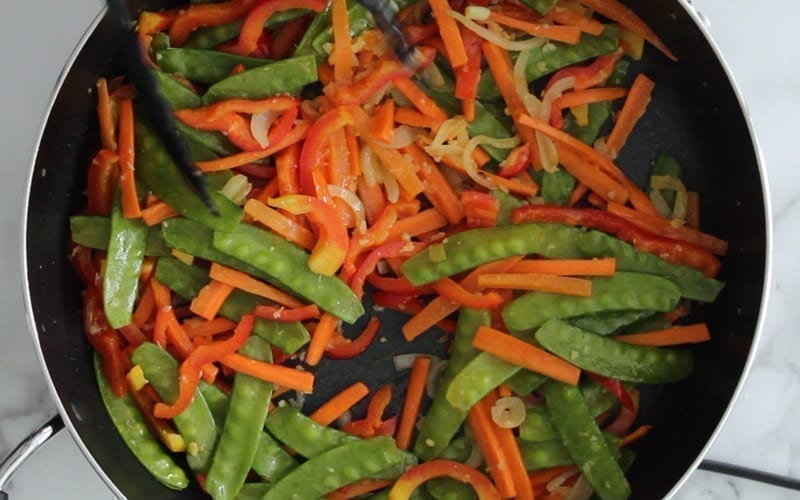 Cooked Singapore noodle vegetables in a pan; includes carrots, onion, garlic, snow peas and bell peppers