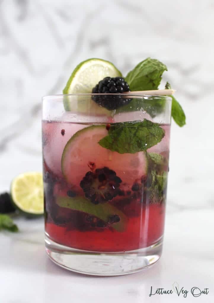Glass of blackberry mojito mocktail with crushed blackberries in the drink along with mint leaves and lime slices