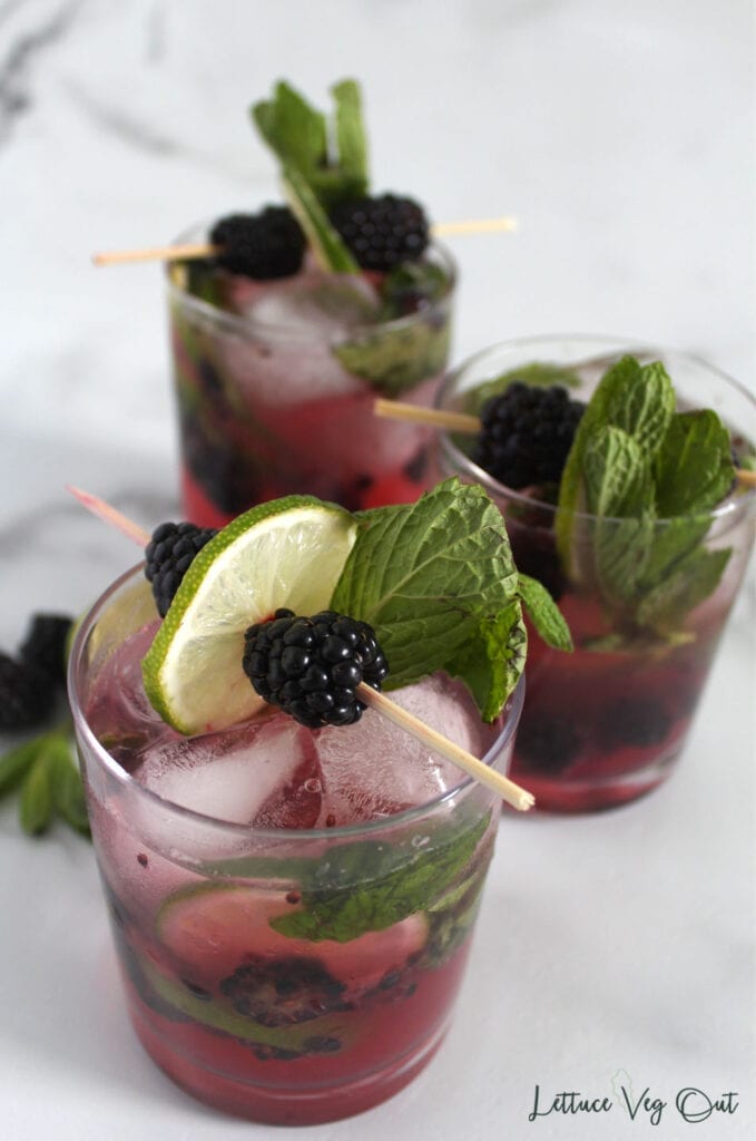 Top view of three glasses of blackberry mocktail with skewers of blackberries and lime slices for garnish