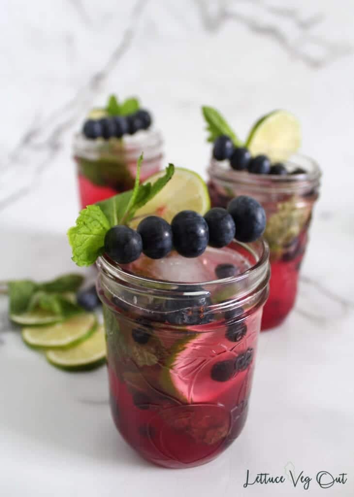 Row of 3 glasses (mason jars) of blueberry mojito mocktails with lime, mint and blueberry decorations