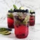 Three small jars of blueberry mojito mocktails with lime slices, fresh mint and fresh blueberries as decoration and garnish (on marble background)