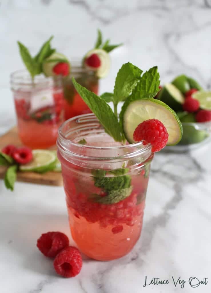 Three mason jar glasses of raspberry mocktails garnished with mint, lime and fresh raspberries
