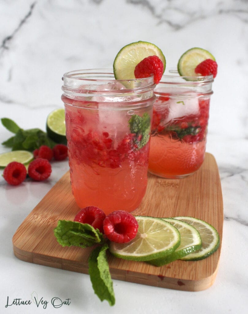 Two glasses of pink raspberry mojito mocktail on wooden board with lime and raspberry garnish