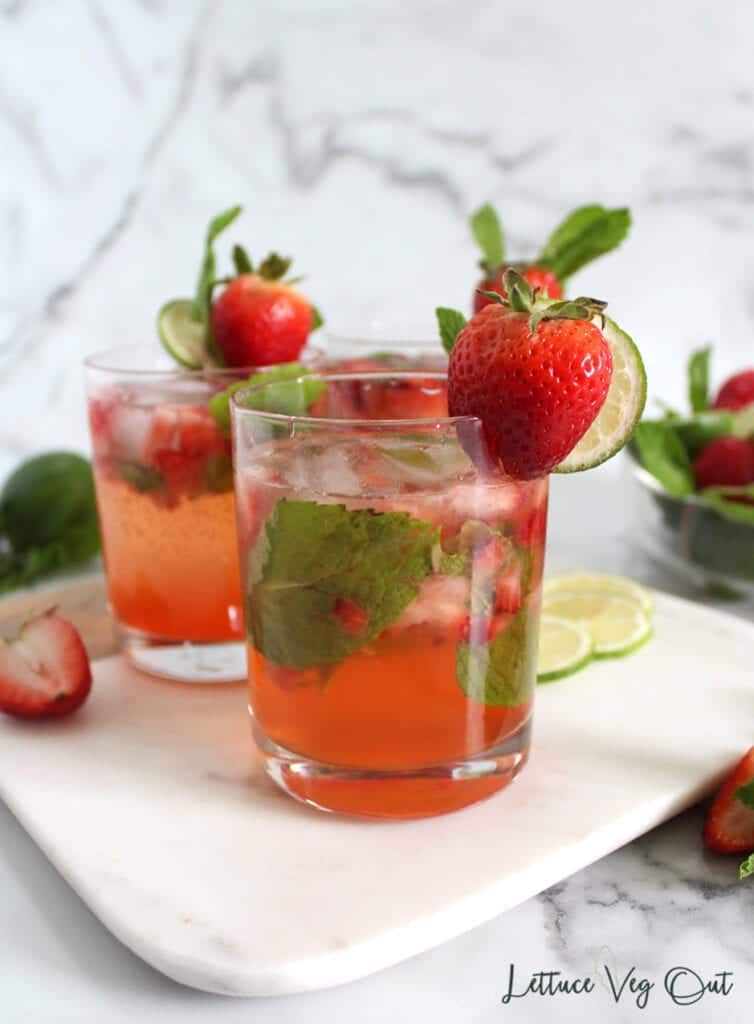 Straight on view of non alcoholic strawberry mojito with lime, mint and whole strawberry garnish on marble board