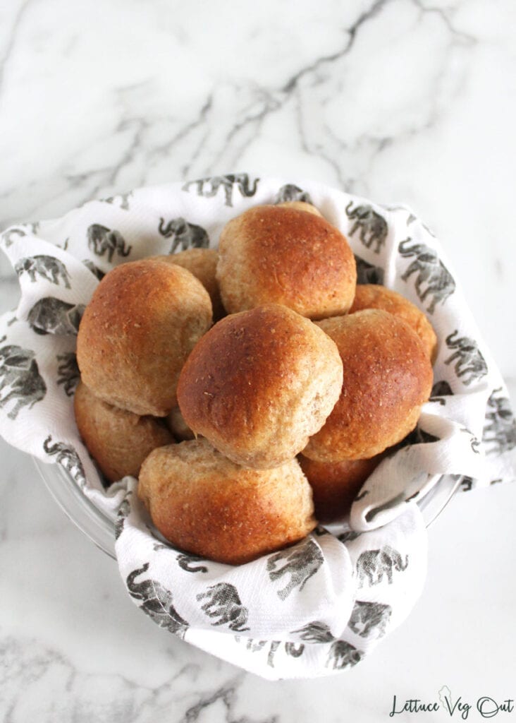 Large bowl lined with towel filled with vegan whole wheat dinner rolls