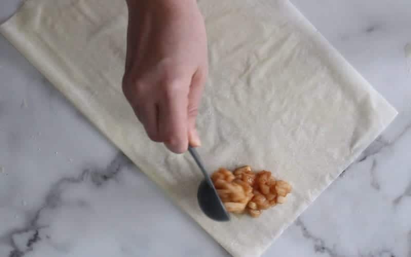 Image of apple turnover being prepared with a scoop of apple filling on phyllo pastry
