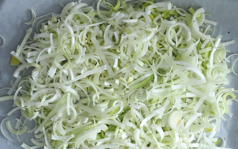 Image of sliced leeks on a parchment covered baking sheet, ready to bake and add into creamy risotto