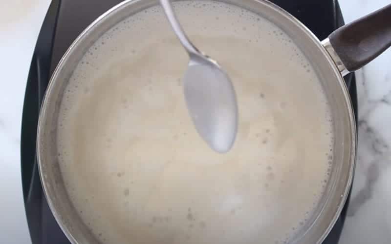 Close-up image of homemade donair sweet sauce in a pot with a spoon covered, showing the ideal sauce consistency.