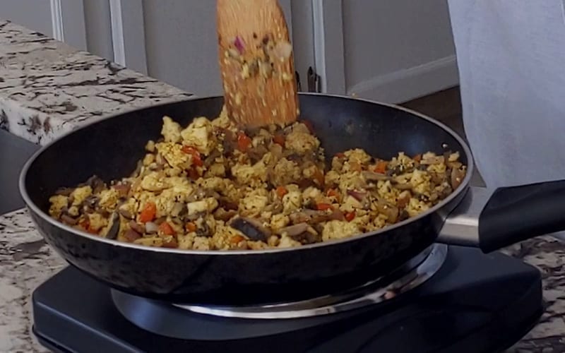 Vegan tofu scramble and veggies combined in a frying pan. Both components will cook together for a few minutes before serving