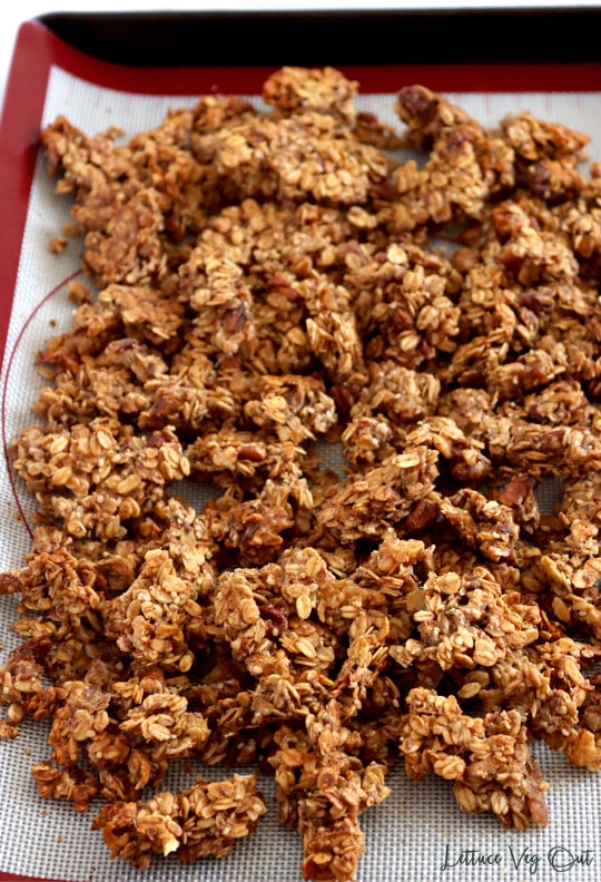 Full baking tray of peanut butter granola with nut clusters. Silicone mat sits on the tray.
