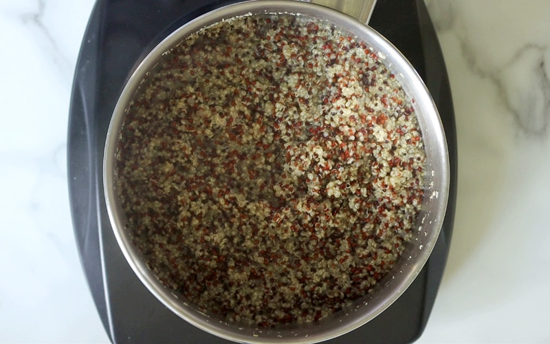 Top view of tri colored quinoa (white, red, black) cooking in metal pot with steam rising up.