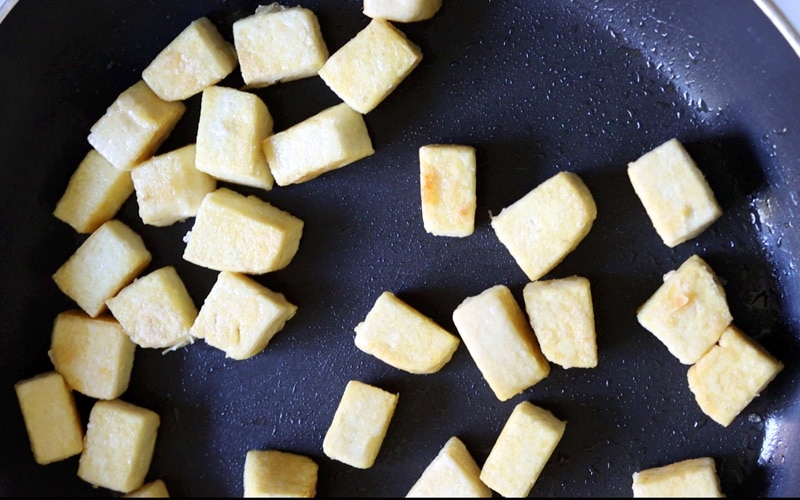Close up of lightly browned (pale yellow) tofu cubes in a pan.