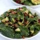 Square cropped image of a white plate full of tossed spinach salad with cucumber, hemp seed and nuts.