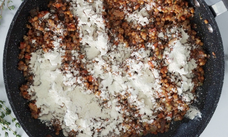 Top view of a pan with vegetable and lentil mixture with flour sprinkled all over the surface of the lentil mix.