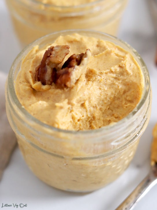 Close up of a small jar of pumpkin mousse with a large spoonful removed, showing the fluffy texture of the mousse.