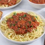 Square cropped image of a close up of a plate of lentil spaghetti sauce over pasta, garnished with chopped parsley.