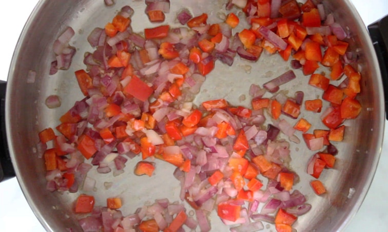 Top view of cooked red bell pepper and red onion in a pot.