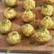 Square cropped image of a wood board topped with mini potatoes that are stuffed with a piped deviled "egg" filling and garnished with parsley, green onion and paprika.