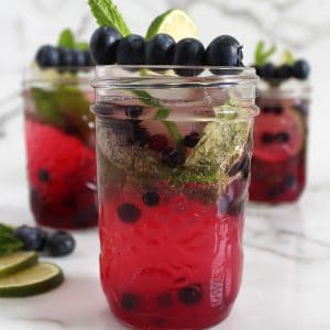 Small mason jar filled with purple blueberry mocktail, blueberries, mint and lime.