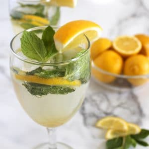 Close up of a wine glass filled with pale yellow lemon and mint mocktail.