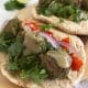Close up of a pita bread wrap topped with green falafel, red onion, tomatoes, cilantro and tahini sauce.