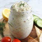 Close up of an overflowing jar of tzatziki sauce garnished with fresh dill.