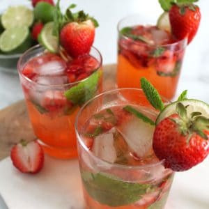 Three glasses of light pink mocktails with strawberries, lime and mint.