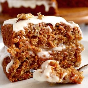 Close up of a slice of double-layer carrot cake with drippy white icing.