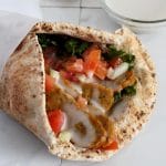 Close up of a pita bread wrap filled with donair "meat", white sauce, tomatoes and onion.