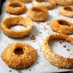 Large quinoa coated onion rings on a parchment-covered baking tray.