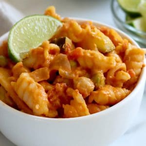 Small white bowl of creamy red curry pasta with lime wedge