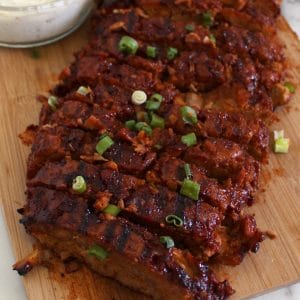 Wood board topped with sliced vegan "ribs" that are garnished with green onion.