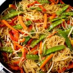 Close up of a large pan filled with prepared singapore noodles and vegetables.