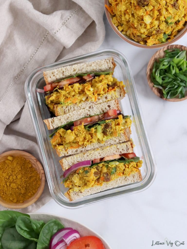 Top view of a few chickpea curry sandwiches in a glass dish with ingredients surrounding dish.