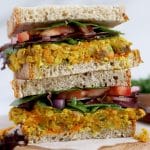 Square cropped close up of a stack of sandwiches filled with curried chickpea salad and vegetables.