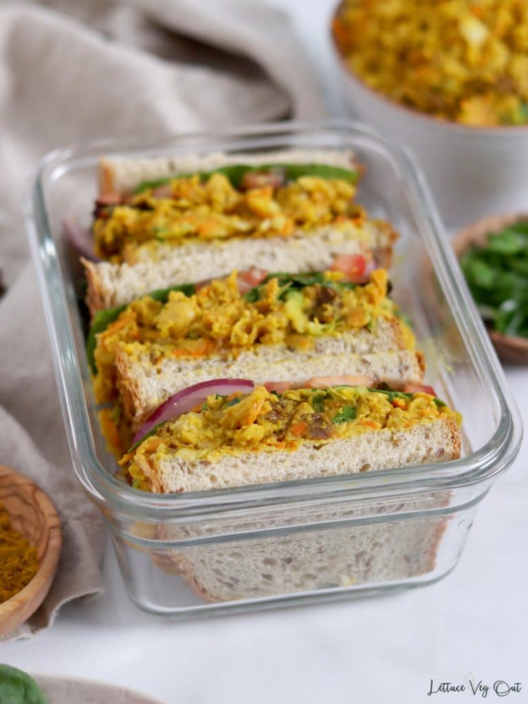 Three curry chickpea sandwiches packed into rectangular glass container.