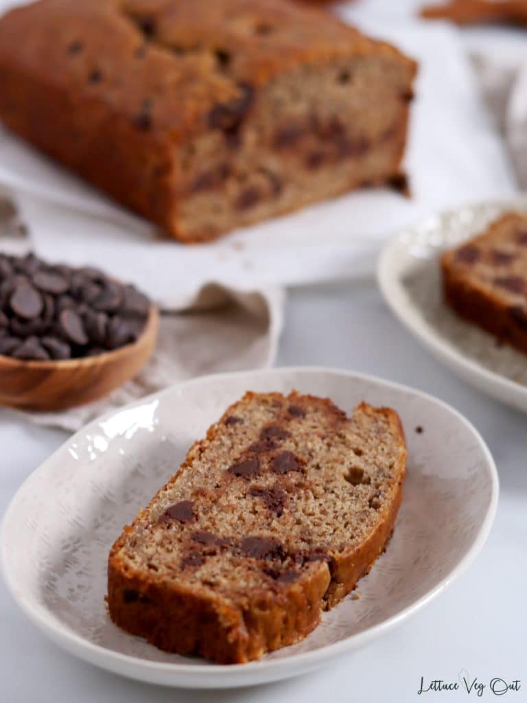 Slice of chocolate chip banana loaf on small plate with rest of loaf in background.
