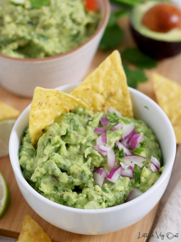 Small bowl of guacamole topped with red onion with corn chips in the dip.