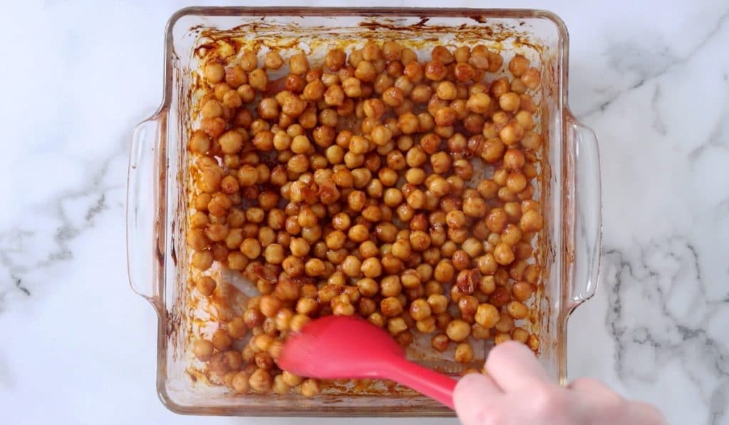 Roasted BBQ chickpeas being stirred in a baking dish.