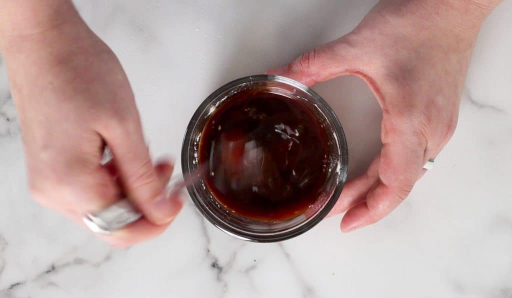 Hands whisking dark sauce in small jar.