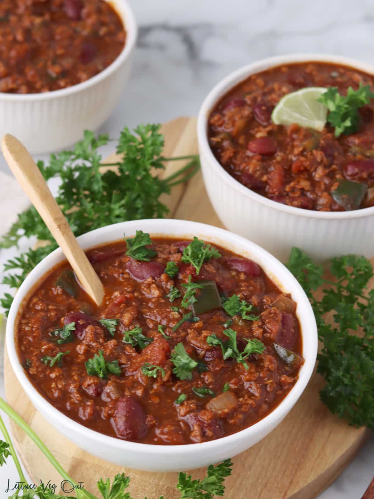 Two bowl of TVP chili on a wood board garnished with chopped herbs and lime slices.