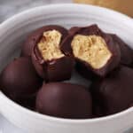 Close up of a bowl with chocolate covered peanut butter balls, bits taken from two balls to show peanut butter inside.