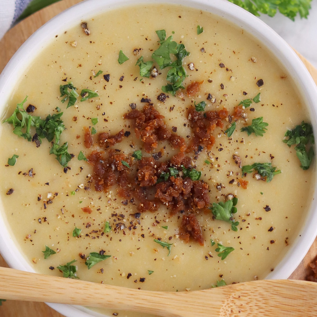 Close up of a bowl of creamy potato soup topped with vegan bacon bits and chives.