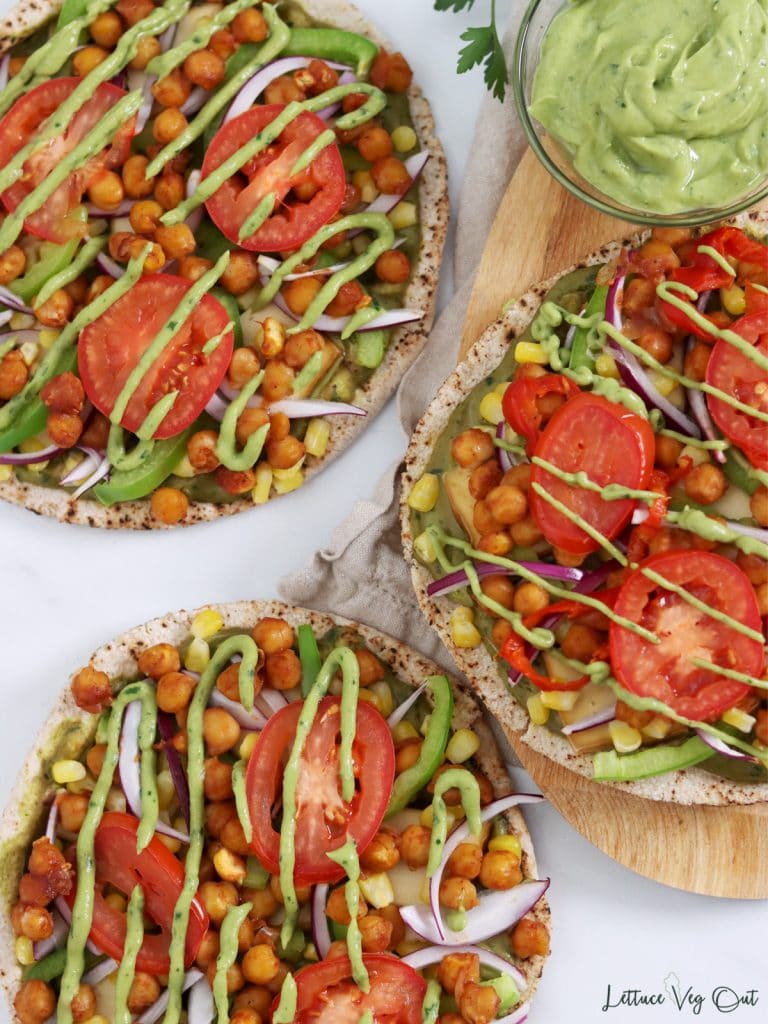 Three small pizzas with a bowl of avocado sauce.