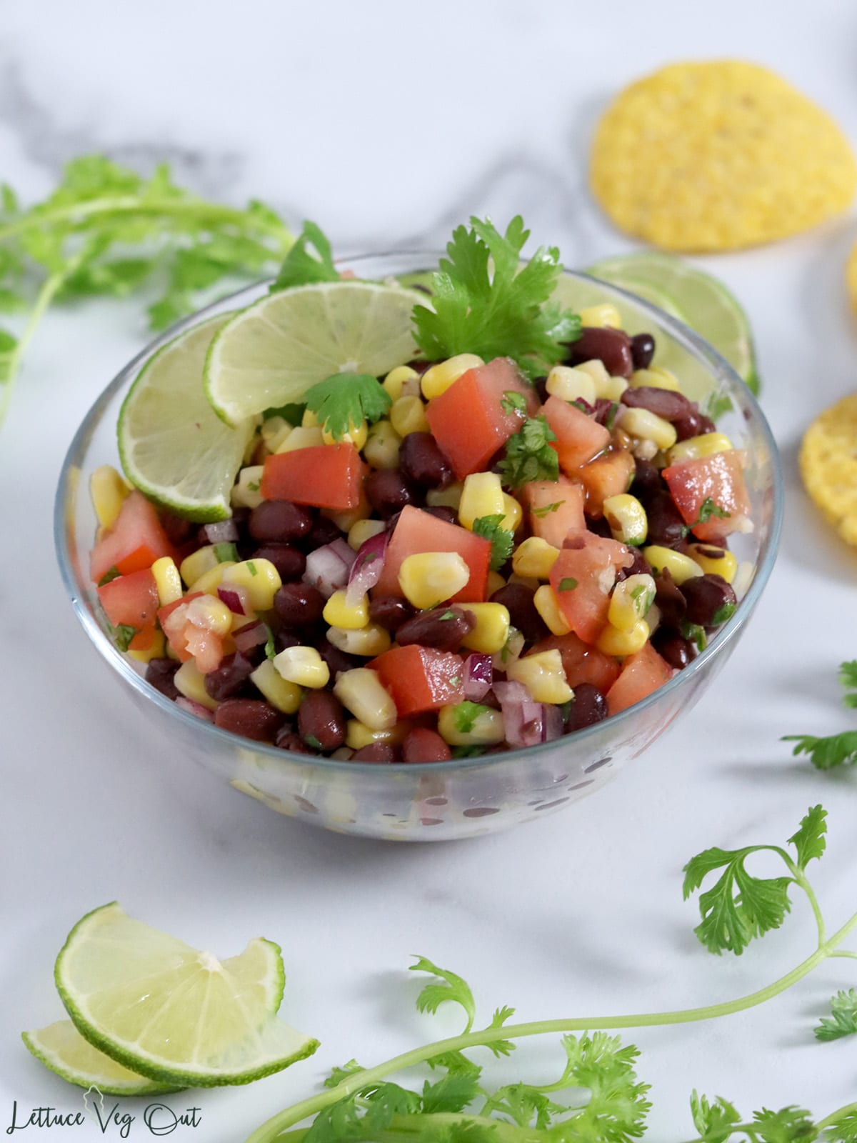 Black bean and corn salsa with tomatoes, lime and cilantro in a glass bowl.