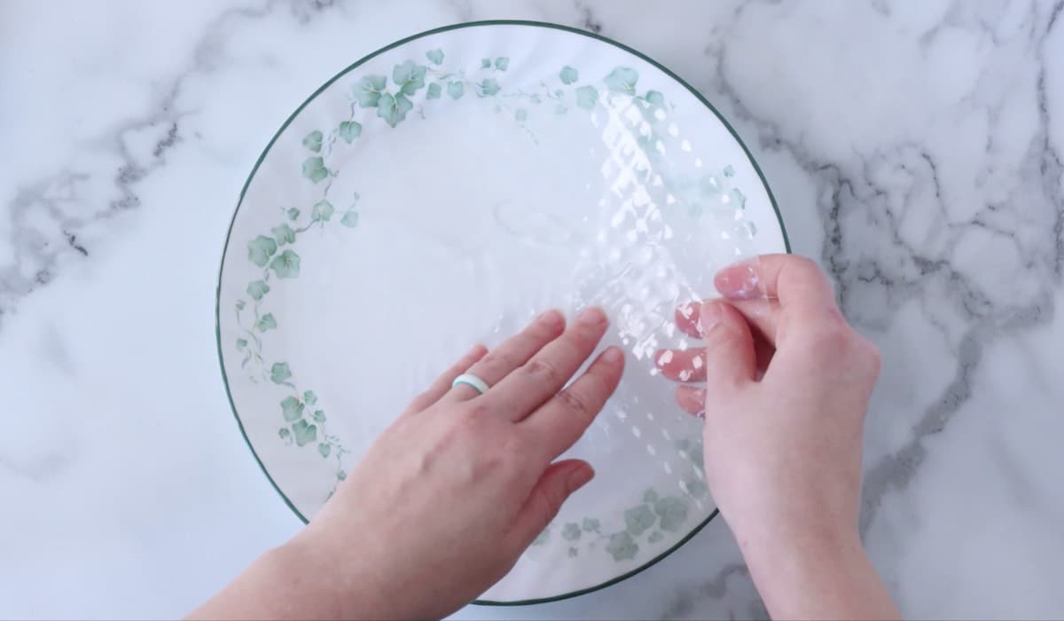 Hands dipping a sheet of rice paper into water on a plate.