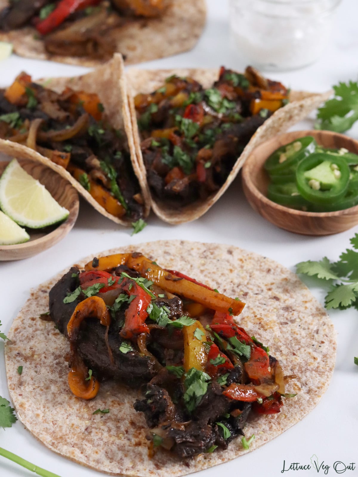 Small tortilla topped with cooked fajitas vegetables (mushroom, onion, pepper) and cilantro garnish.