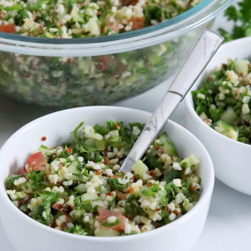 Close up of three partially-cropped bowls of tabbouleh (bulgur, parsley, tomato, red onion).