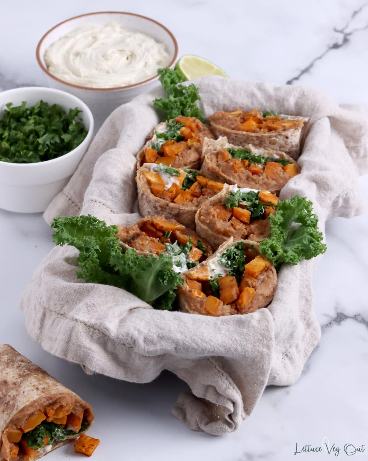Burritos filled with sweet potato, refried beans and kale cut in half in a bowl.